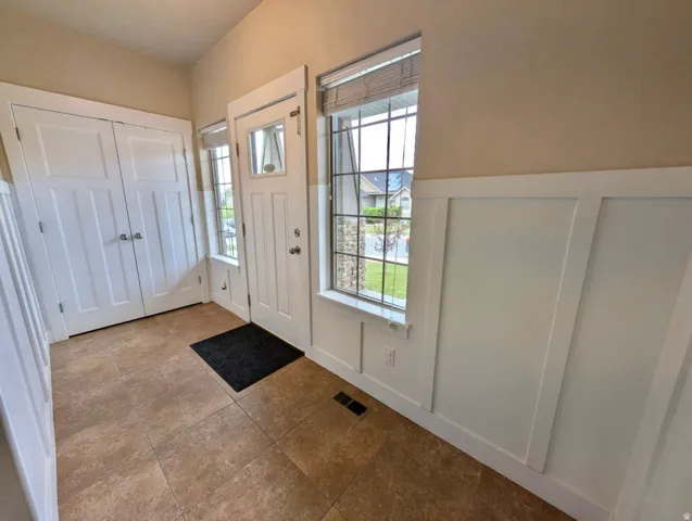 Entryway featuring ceramic tile flooring, classic board and batten wainscoting, white trim, a solid panel entry door with glass inserts, and a dual-door closet with panel detailing