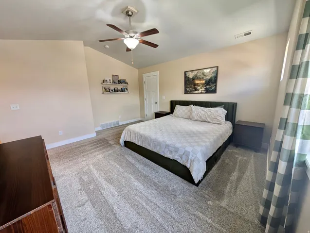 Spacious room featuring vaulted ceilings, a ceiling fan, light-toned wall paint, and plush carpet flooring