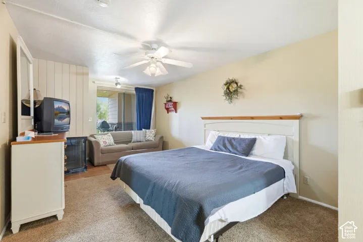 Carpeted interior space featuring a ceiling fan, light-toned walls, and a sliding glass door leading to an exterior patio