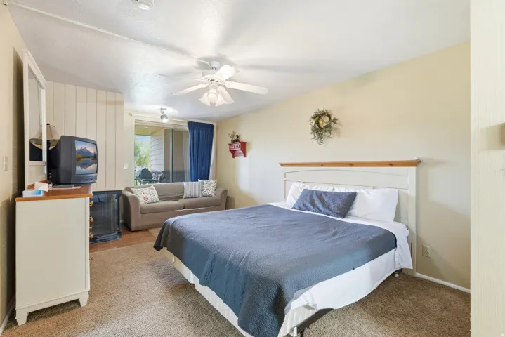 Carpeted interior space featuring a ceiling fan, light-toned walls, and a sliding glass door leading to an exterior patio