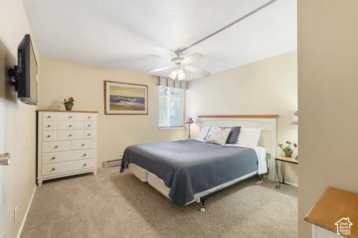 Carpeted bedroom with a ceiling fan, window with horizontal blinds, and a wall-mounted television bracket