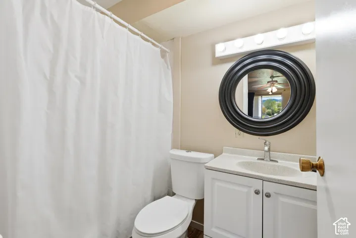 Bathroom featuring a white toilet, white vanity with integrated sink, chrome faucet, and a round black framed mirror
