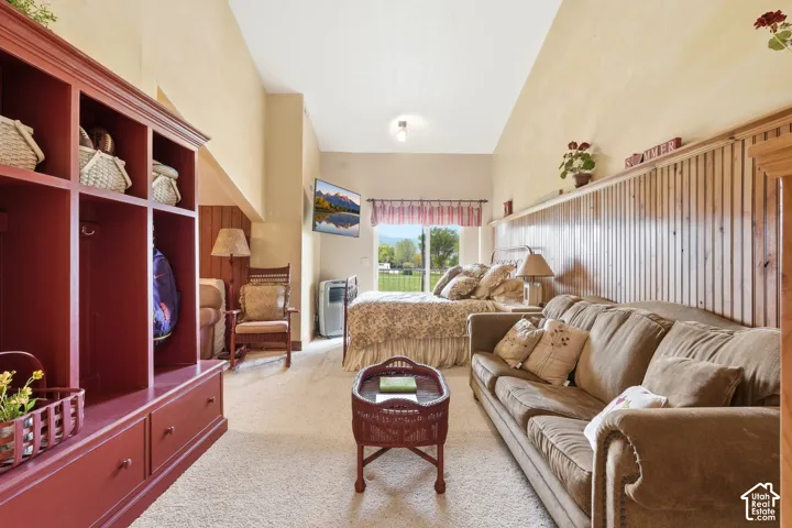Vaulted ceilings accent this expansive room featuring carpet flooring, built-in shelving, wood-paneled walls, and a large window