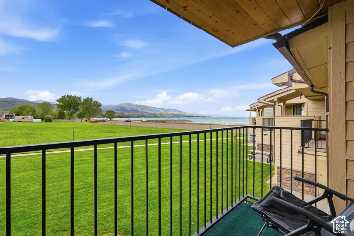 Balcony with black metal railing overlooking a broad green expanse, a tranquil body of water, and distant mountains