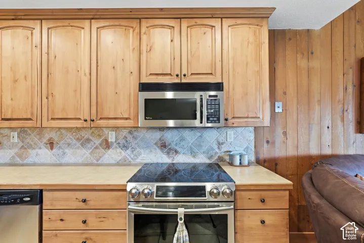 Kitchen featuring custom wood cabinetry, tiled backsplash, stainless steel microwave, stainless steel range with electric cooktop, and light-toned countertops