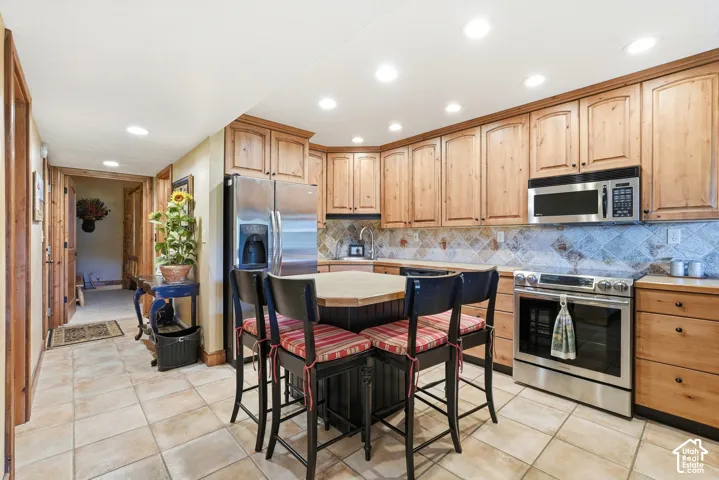 Kitchen featuring natural wood cabinetry, stainless steel appliances, recessed lighting, and a tile backsplash