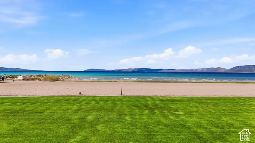 Expansive green lawn bordering a sandy beach and a body of water with distant mountains