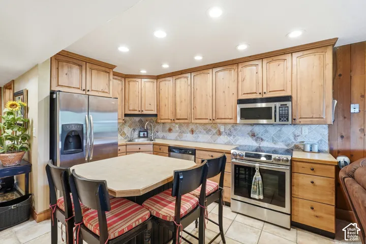 Kitchen featuring light wood cabinetry, stainless steel appliances, a center island with seating, a tiled backsplash, and recessed lighting