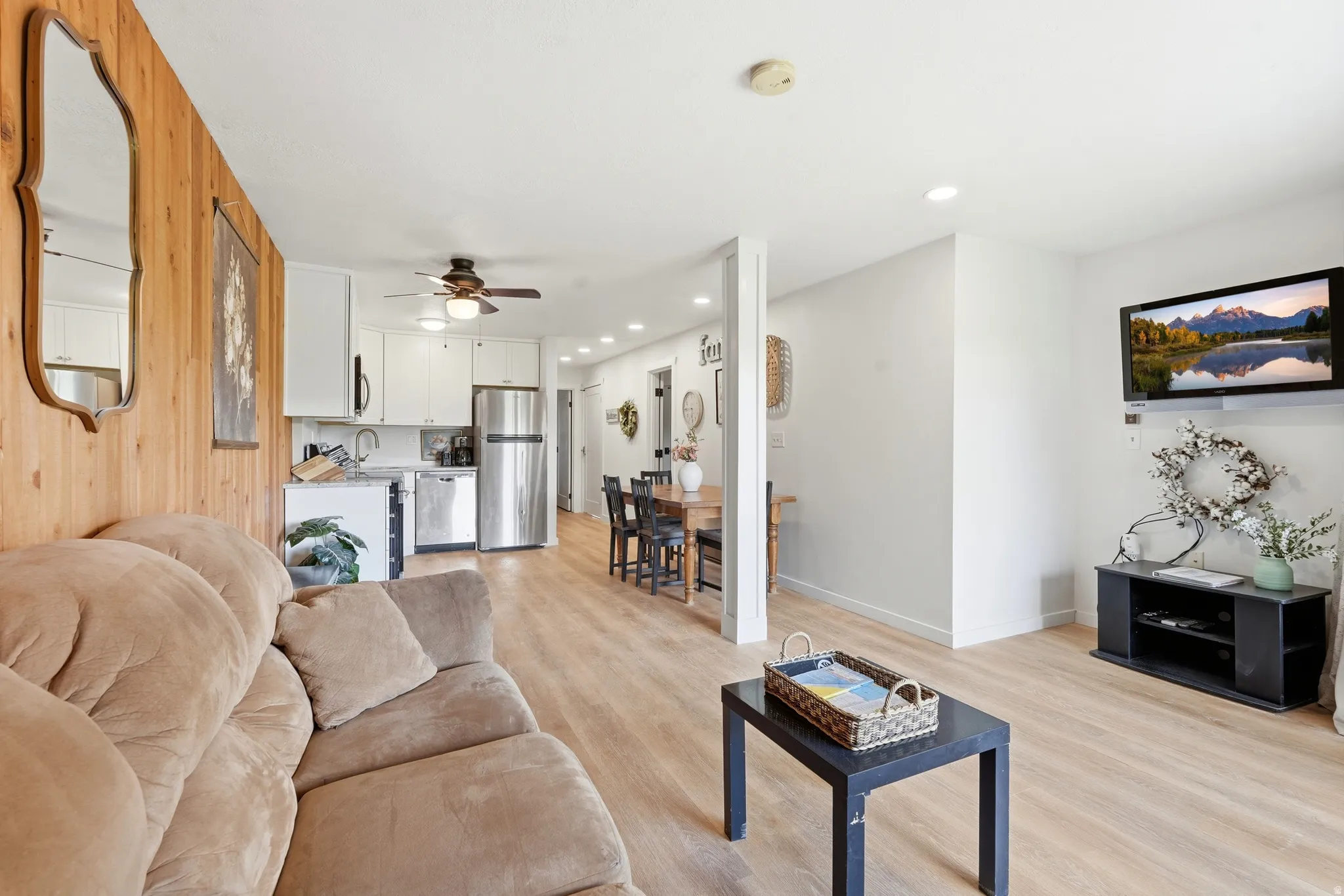 Open-concept living area featuring wood-finish flooring throughout, a wood-paneled accent wall, recessed lighting, and a ceiling fan
