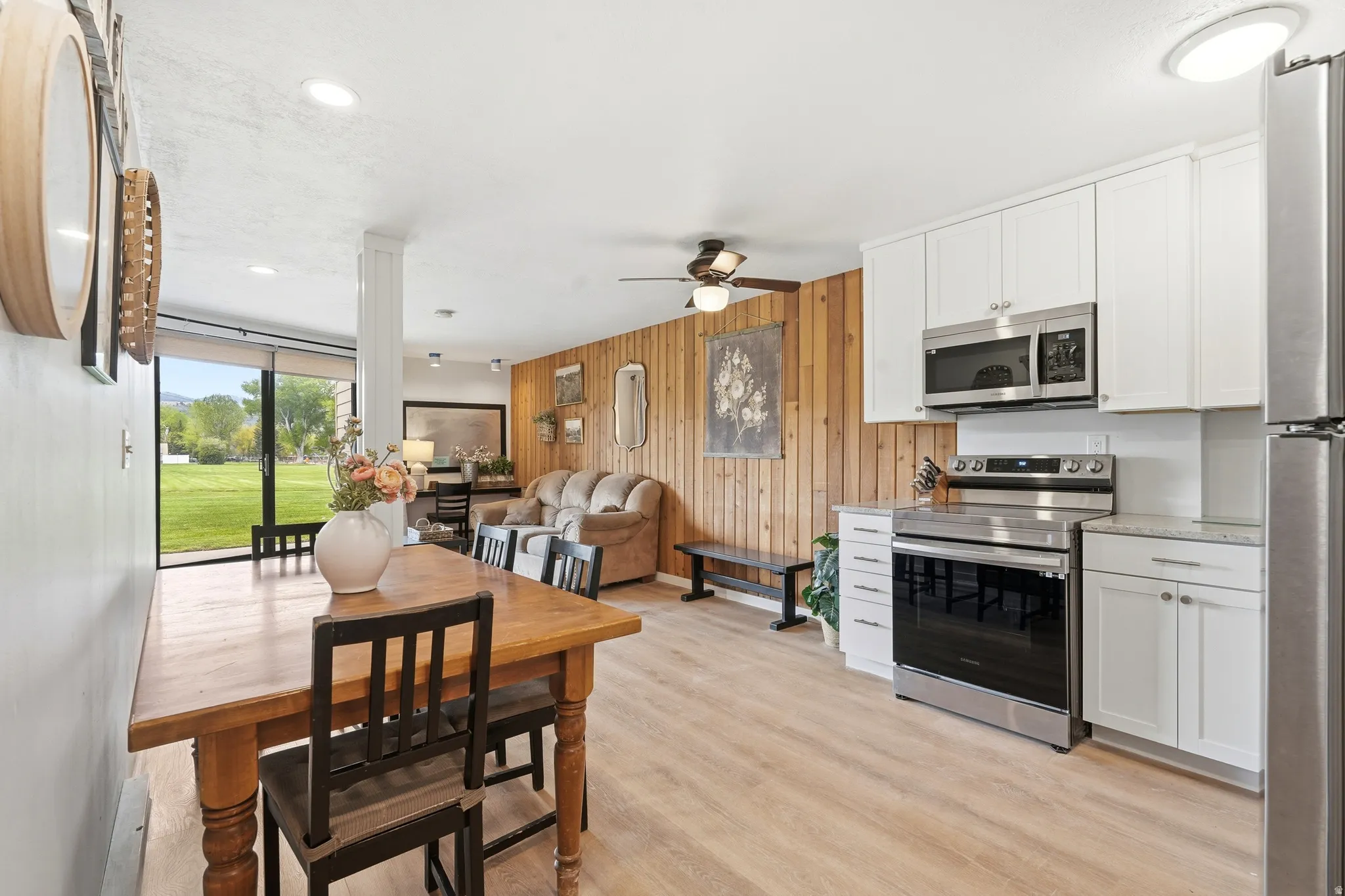 Open-concept living space featuring wood-finish flooring, a kitchen with white cabinetry and stainless steel appliances, and a living area with wood paneling