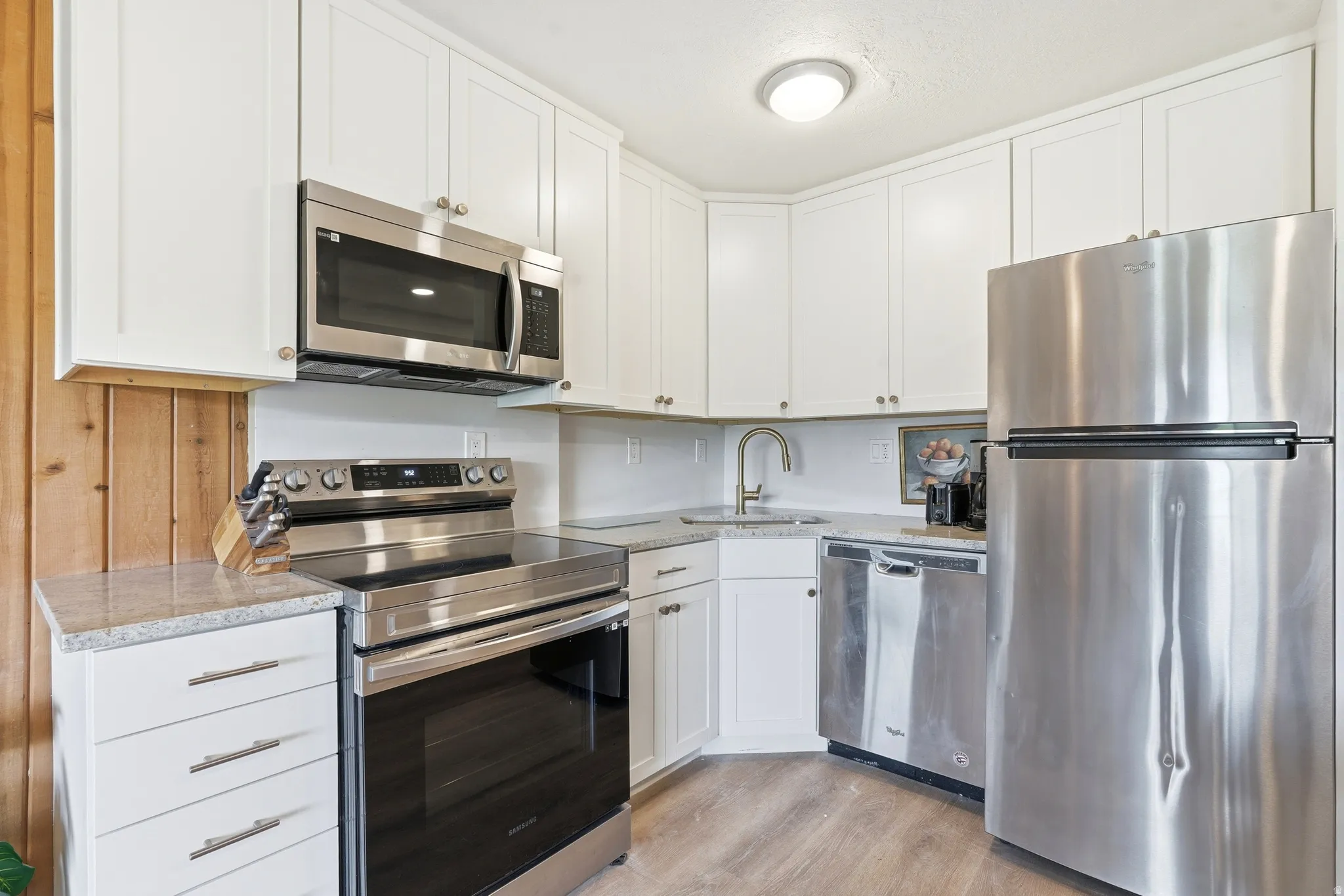 Modern kitchen featuring white shaker cabinetry, stainless steel appliances, speckled countertops, and wood-finish flooring