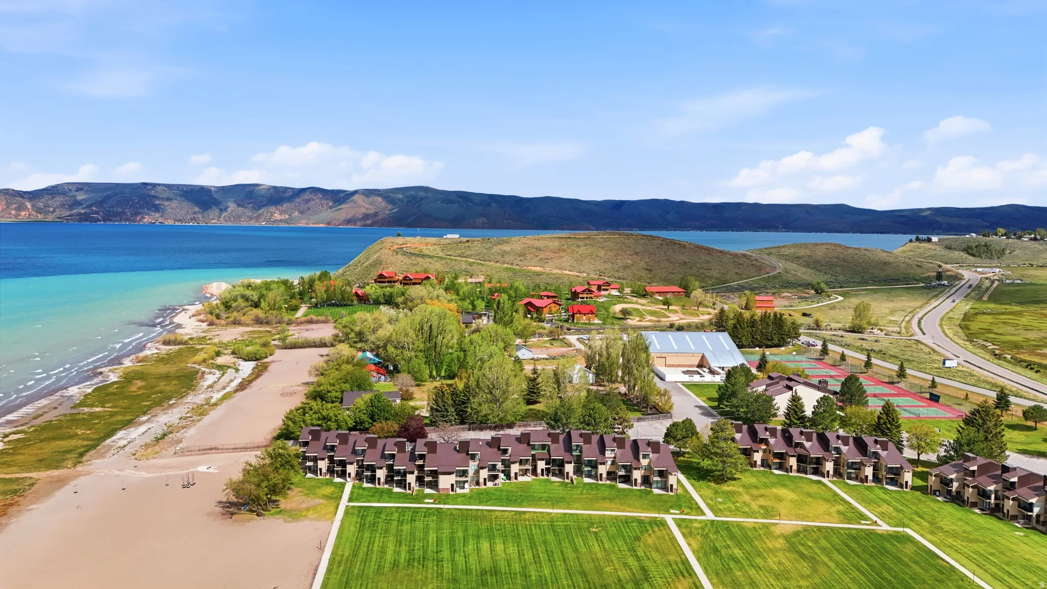 Expansive waterside property featuring multiple residential structures, large grassy areas, and visible tennis courts