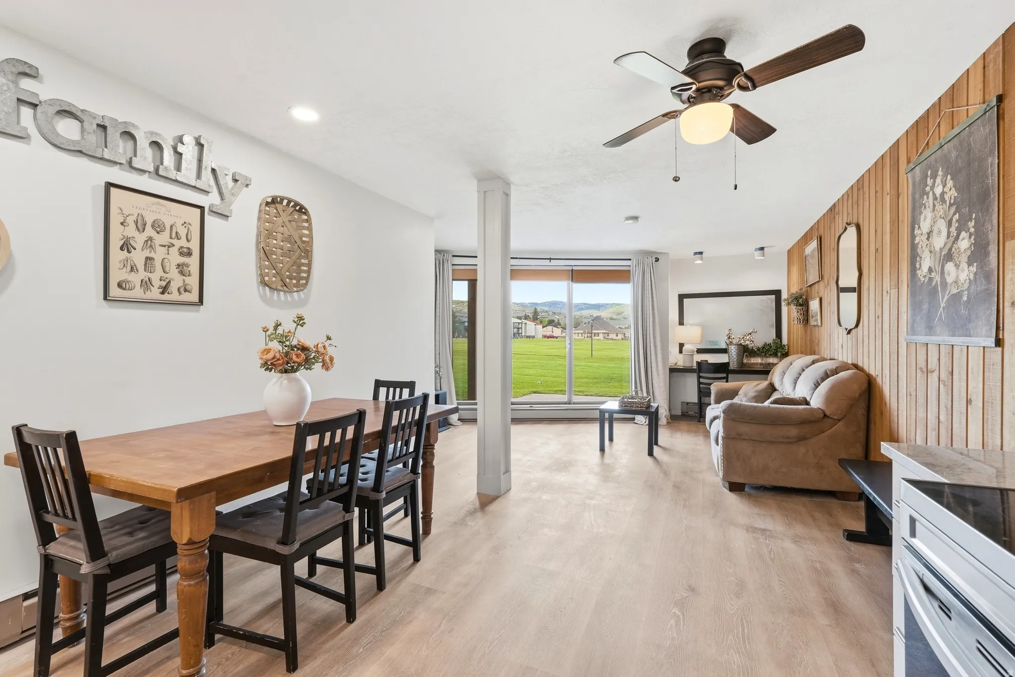 Open-concept living space featuring wood-finish flooring, a full-wall window, and a ceiling fan with integrated lighting