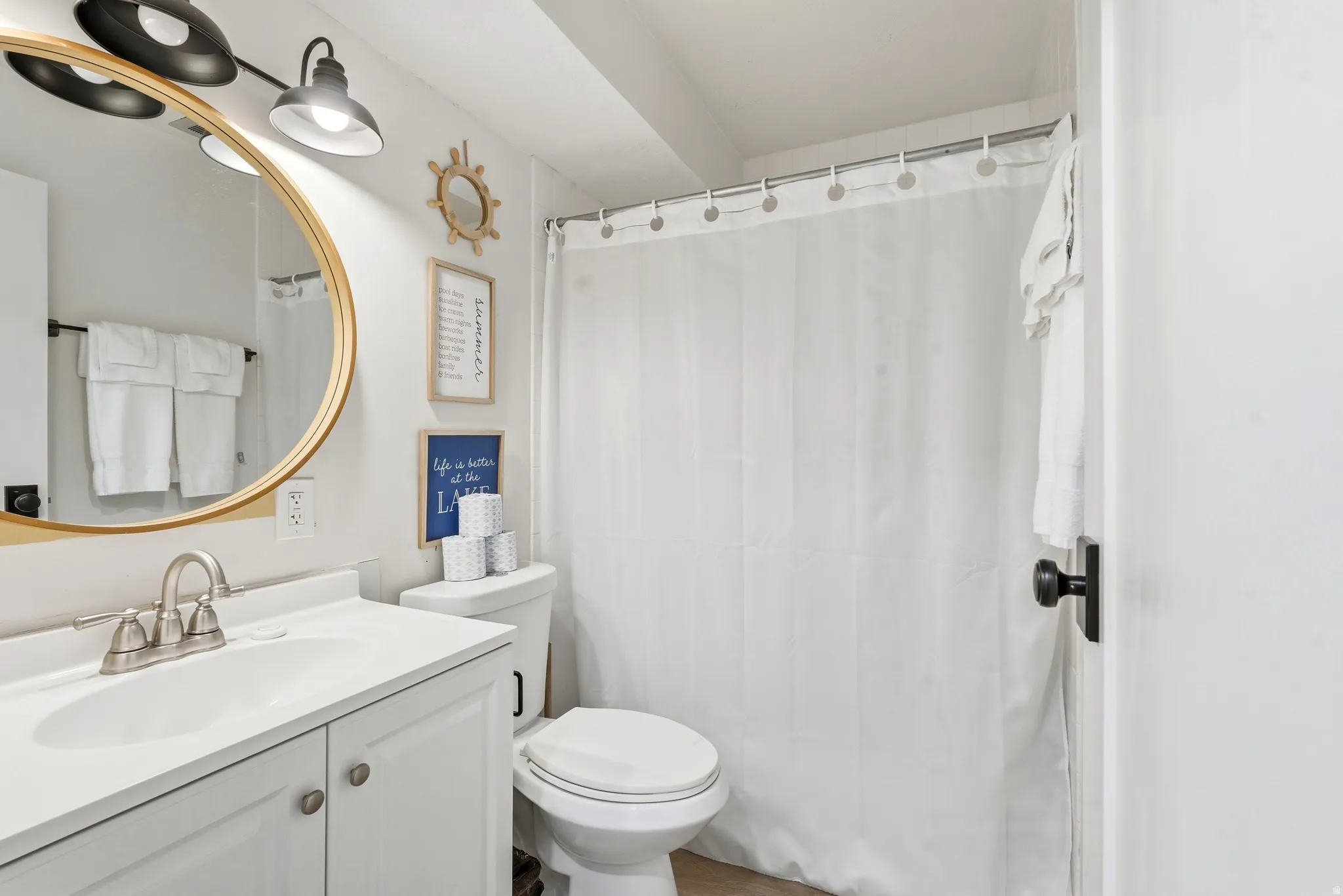 Bathroom featuring a white vanity with a single basin sink, brushed nickel faucet, and a round gold-framed mirror