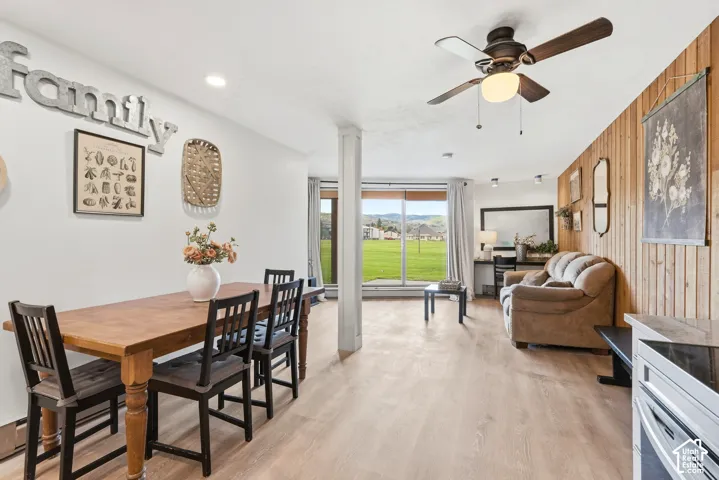 Open-concept living space featuring wood-finish flooring, a full-wall window, and a ceiling fan with integrated lighting