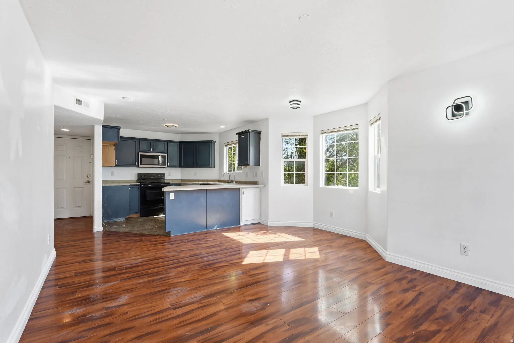 Open-concept living area featuring rich wood-finish flooring and a kitchen with blue cabinetry and a stainless steel microwave