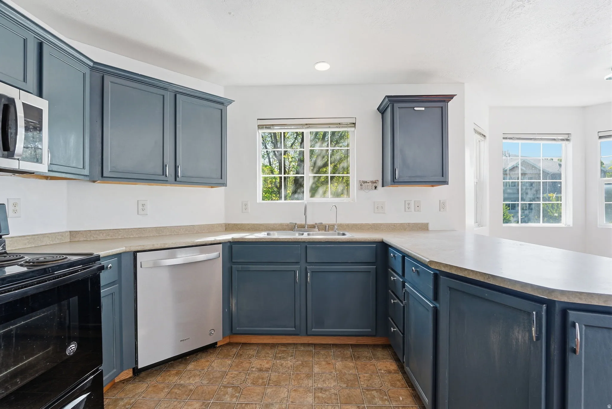 Kitchen featuring blue shaker-style cabinetry, a built-in stainless steel dishwasher, and a double basin sink
