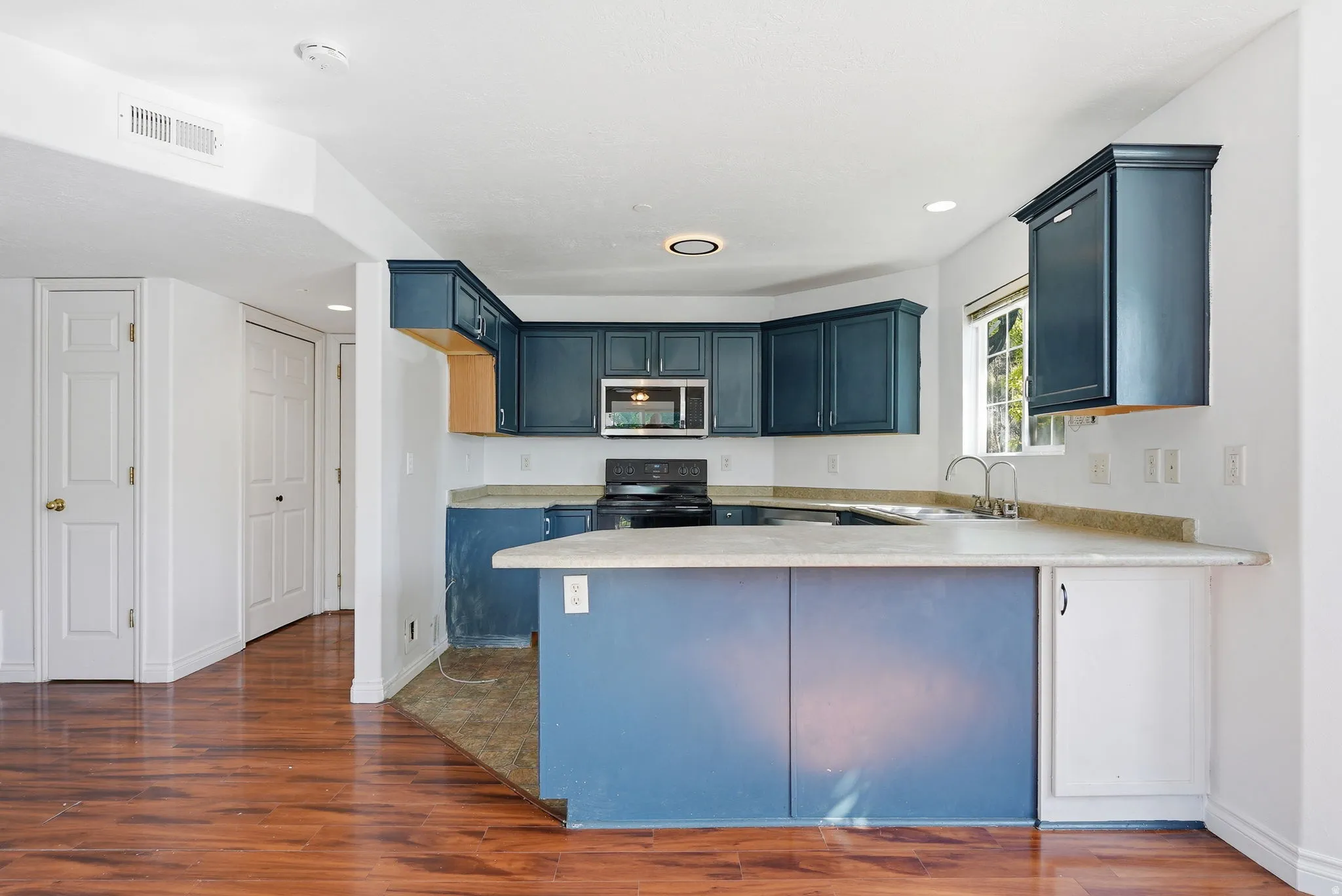 Modern kitchen featuring blue cabinetry, light-toned countertops, a stainless steel microwave, and wood-finish flooring