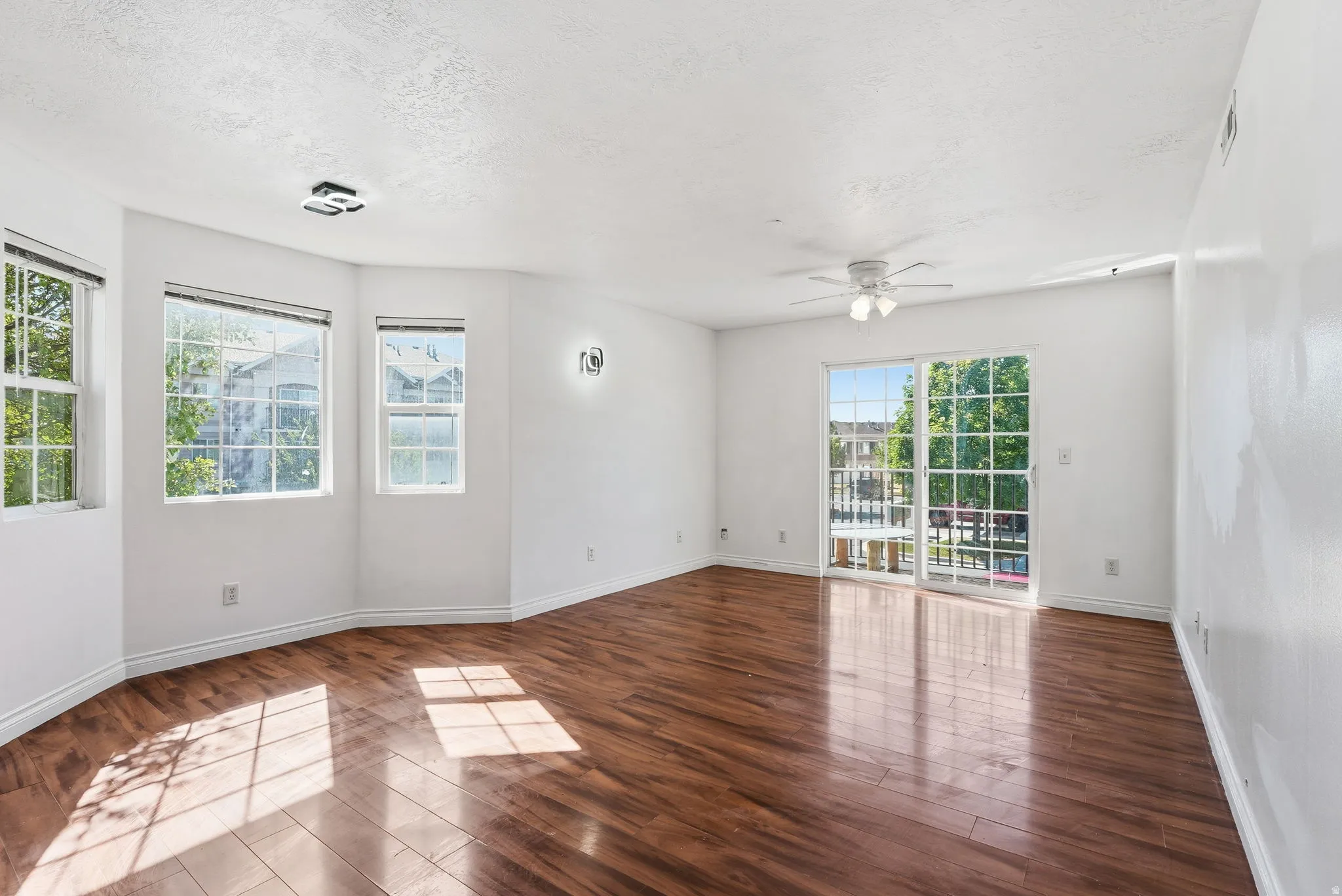Spacious room featuring wood-finish flooring, white walls, and multiple windows