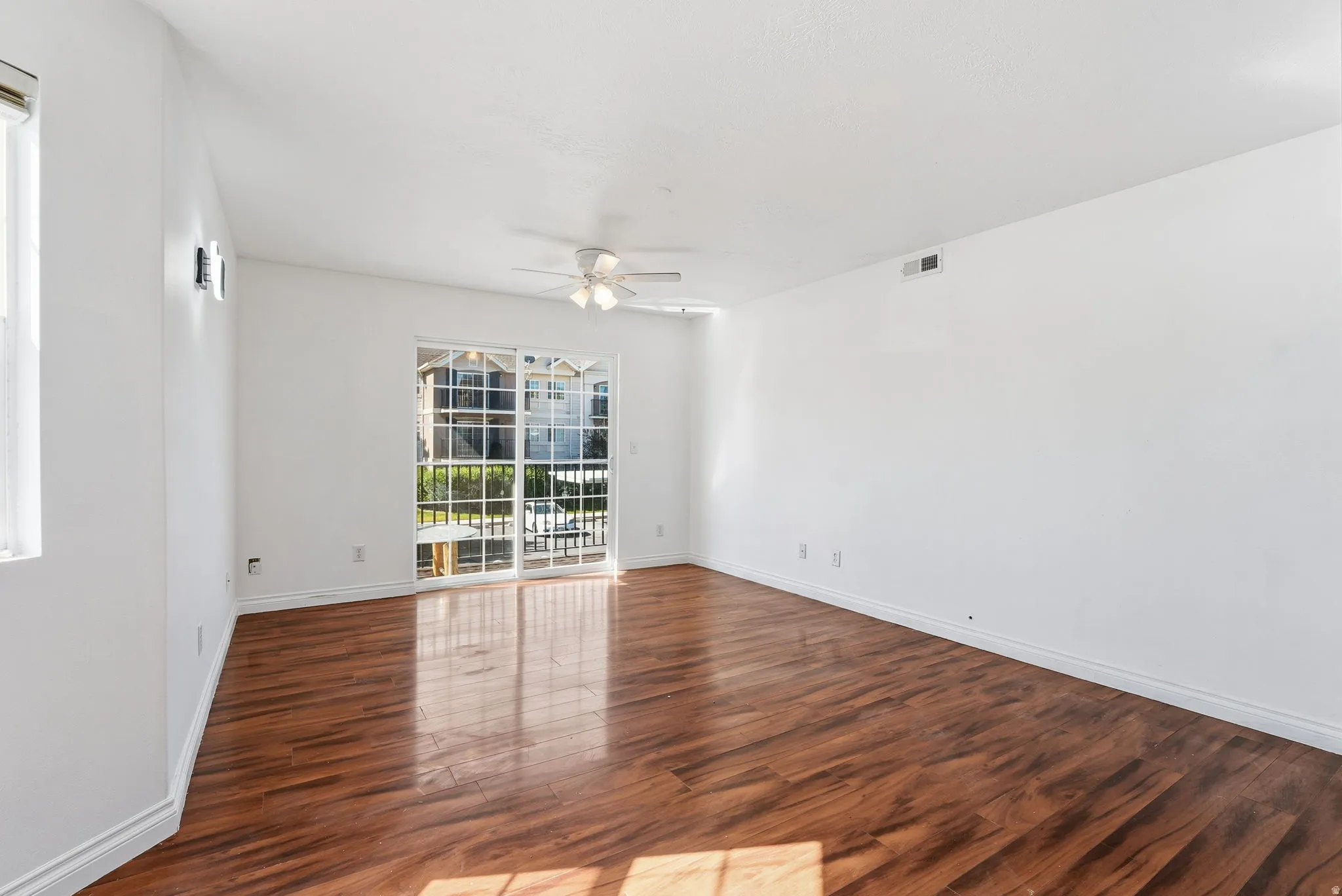 Bright open-concept interior featuring wood-finish flooring, white walls, and a white ceiling fan