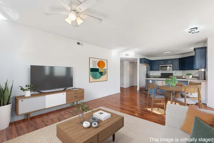 Open-concept living area featuring wood-finish flooring, white walls, and a ceiling fan