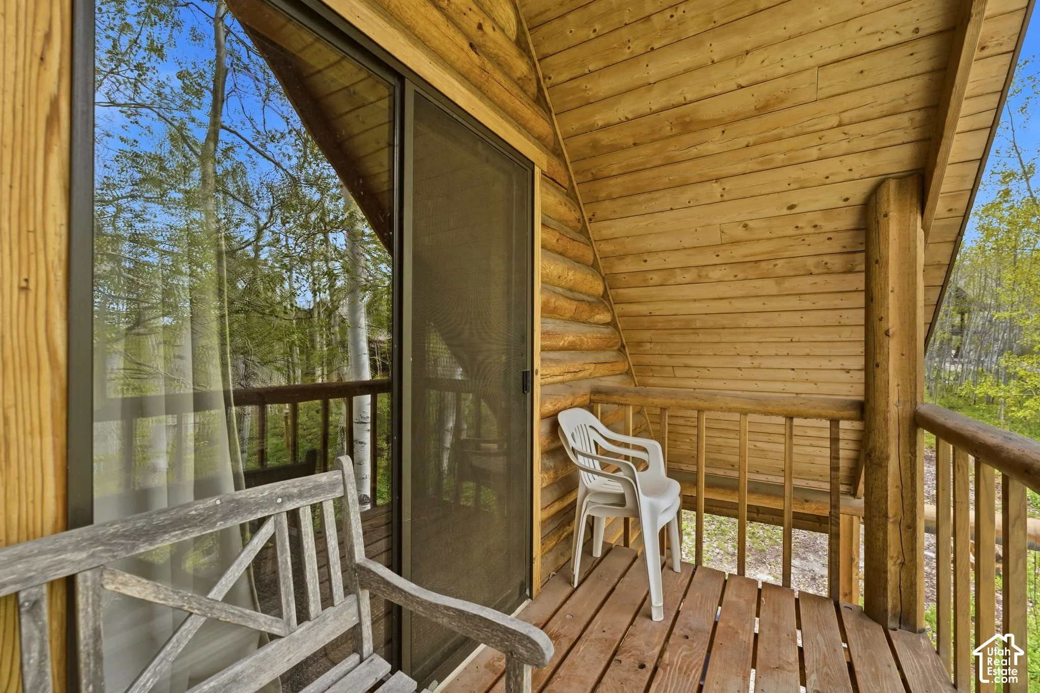 Wood-clad balcony featuring a sliding glass door with screen, natural wood railing, log column support, and plank wood flooring