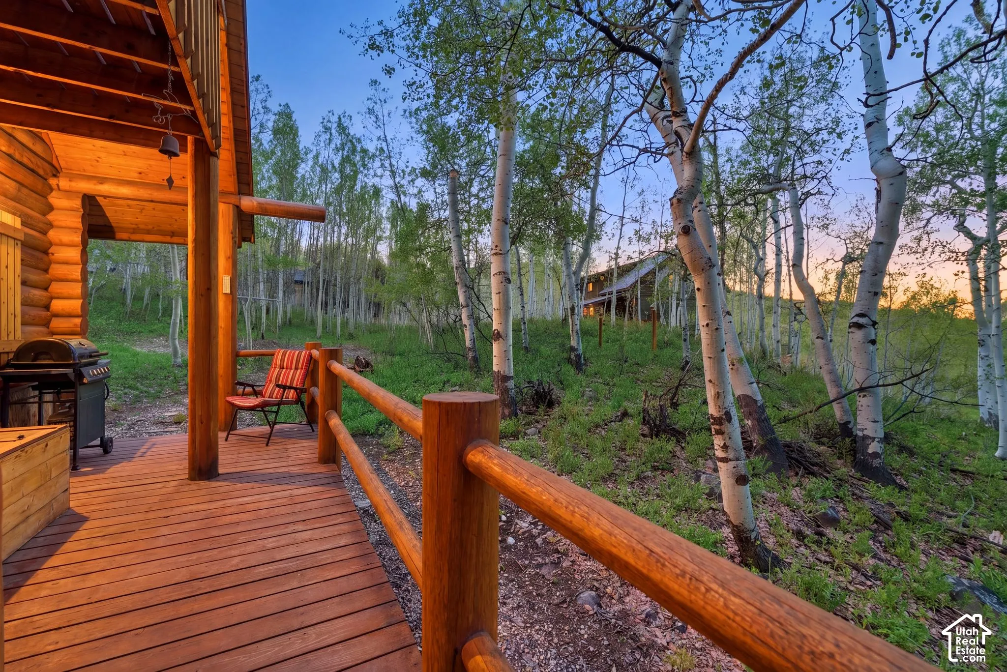 Expansive wood deck with log railing and column, featuring a log cabin exterior and natural surroundings with mature trees