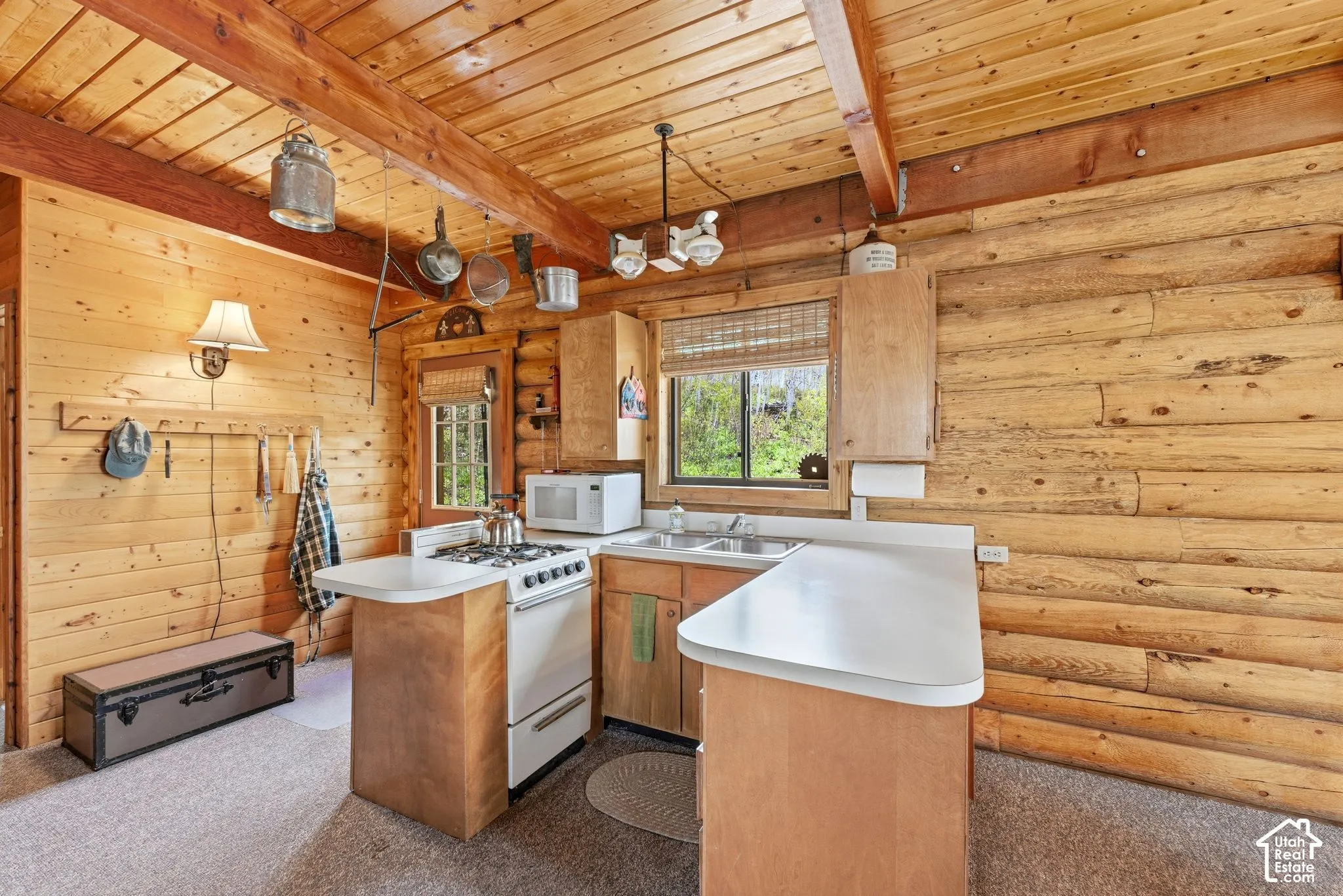 Wood-paneled kitchen featuring log walls, wood-finish flooring, and exposed ceiling beams