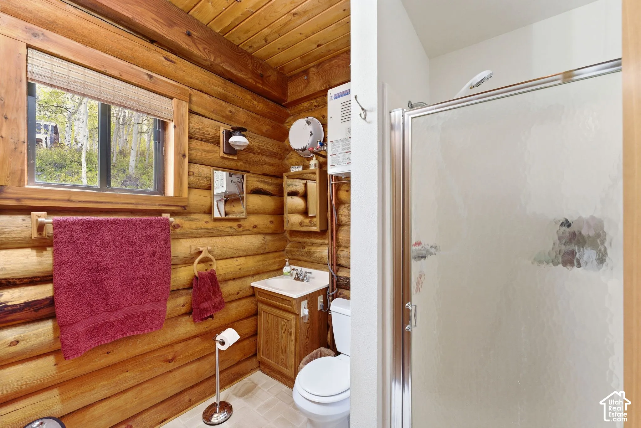Bathroom featuring a glass-enclosed shower, wood-paneled walls and ceiling, a single-sink vanity with a wood cabinet, and a window with a woven wood blind