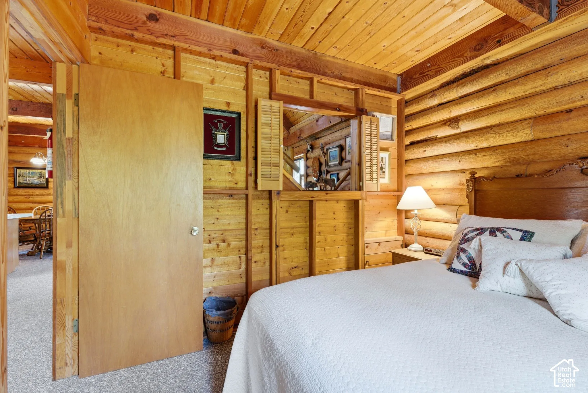 Wood-paneled room featuring a log wall, exposed wood beam ceiling, and a built-in wood-frame opening with louvered shutters