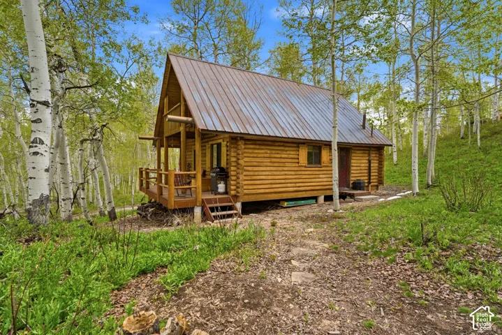 Log cabin exterior featuring a metal roof, front porch, log siding, and surrounding deciduous trees