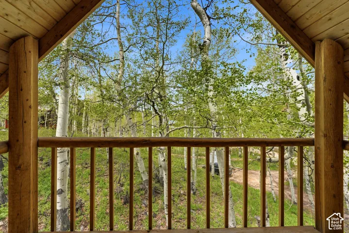 Wood-finish balcony with log-style railing and ceiling, overlooking a forested landscape with mature trees and natural ground cover