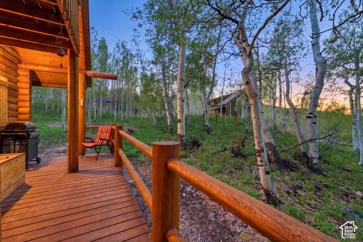 Expansive wood deck with log railing and column, featuring a log cabin exterior and natural surroundings with mature trees