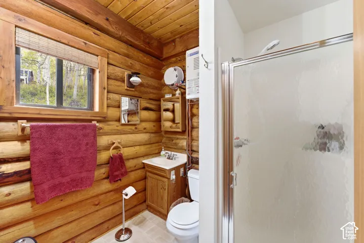 Bathroom featuring a glass-enclosed shower, wood-paneled walls and ceiling, a single-sink vanity with a wood cabinet, and a window with a woven wood blind