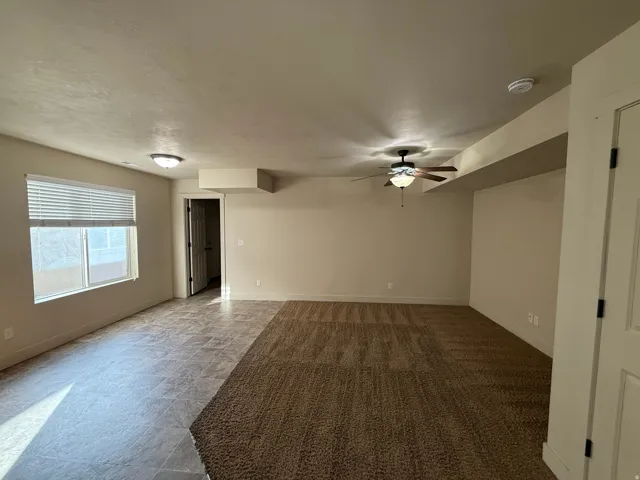 Unit C - Expansive interior space featuring a dual-textured flooring, a ceiling fan with integrated lighting, a large window with horizontal blinds, and recessed lighting fixtures