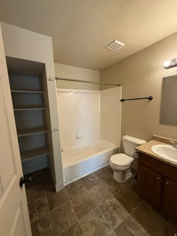 Unit C - Bathroom featuring a bathtub with a white surround, built-in shelving, a toilet, a vanity with a countertop, and tile flooring