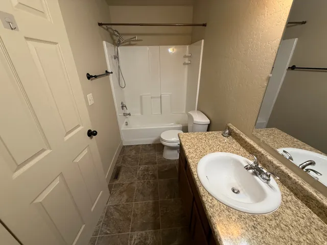 Unit B - Bathroom featuring a single vanity with an integrated sink, a full-width mirror, and a shower-over-tub combination with a white surround