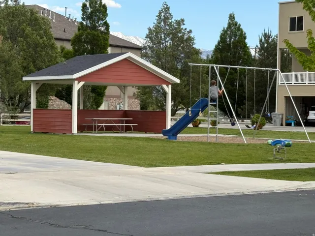 Community green space featuring a red and white gazebo with a picnic table, a swing set with a slide, and mature landscaping
