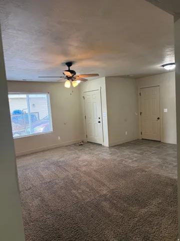 Unit A - Carpeted living area with a ceiling fan light fixture, recessed lighting, and a large window with blinds