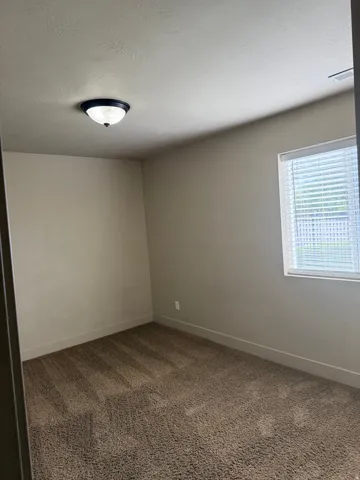 Unit A - Room featuring neutral wall paint, textured ceiling, brown carpet flooring, and a white window with blinds