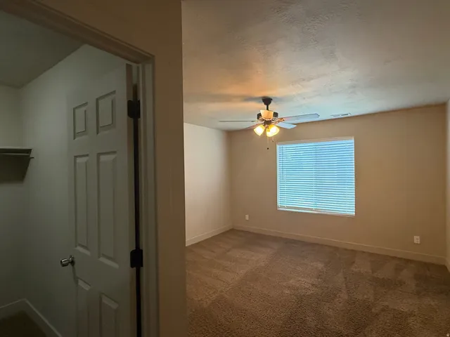 Unit A - Carpeted room featuring a ceiling fan with integrated lighting, a window with horizontal blinds, and a paneled door providing access to a closet with a built-in shelf