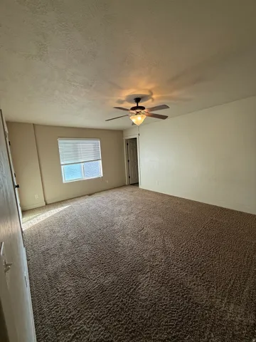 Unit C - Spacious room featuring neutral carpeting, a ceiling fan with integrated lighting, and a window with blinds