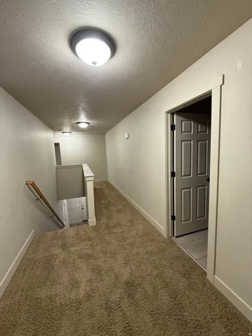 Unit C - Carpeted hallway featuring a staircase with a wooden handrail, flush-mount lighting, and a paneled door opening to tile flooring