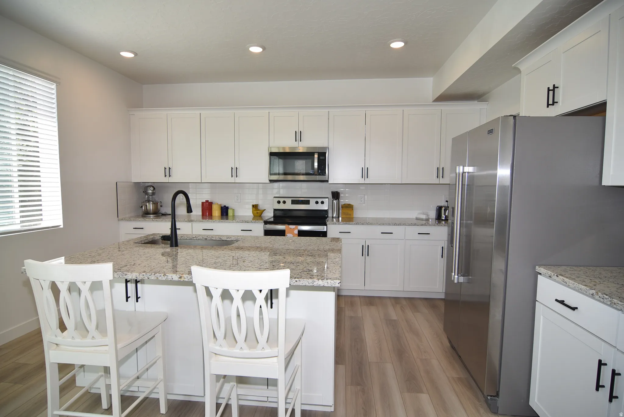 Modern kitchen featuring white shaker cabinetry, stainless steel appliances, speckled countertops, and wood-finish flooring