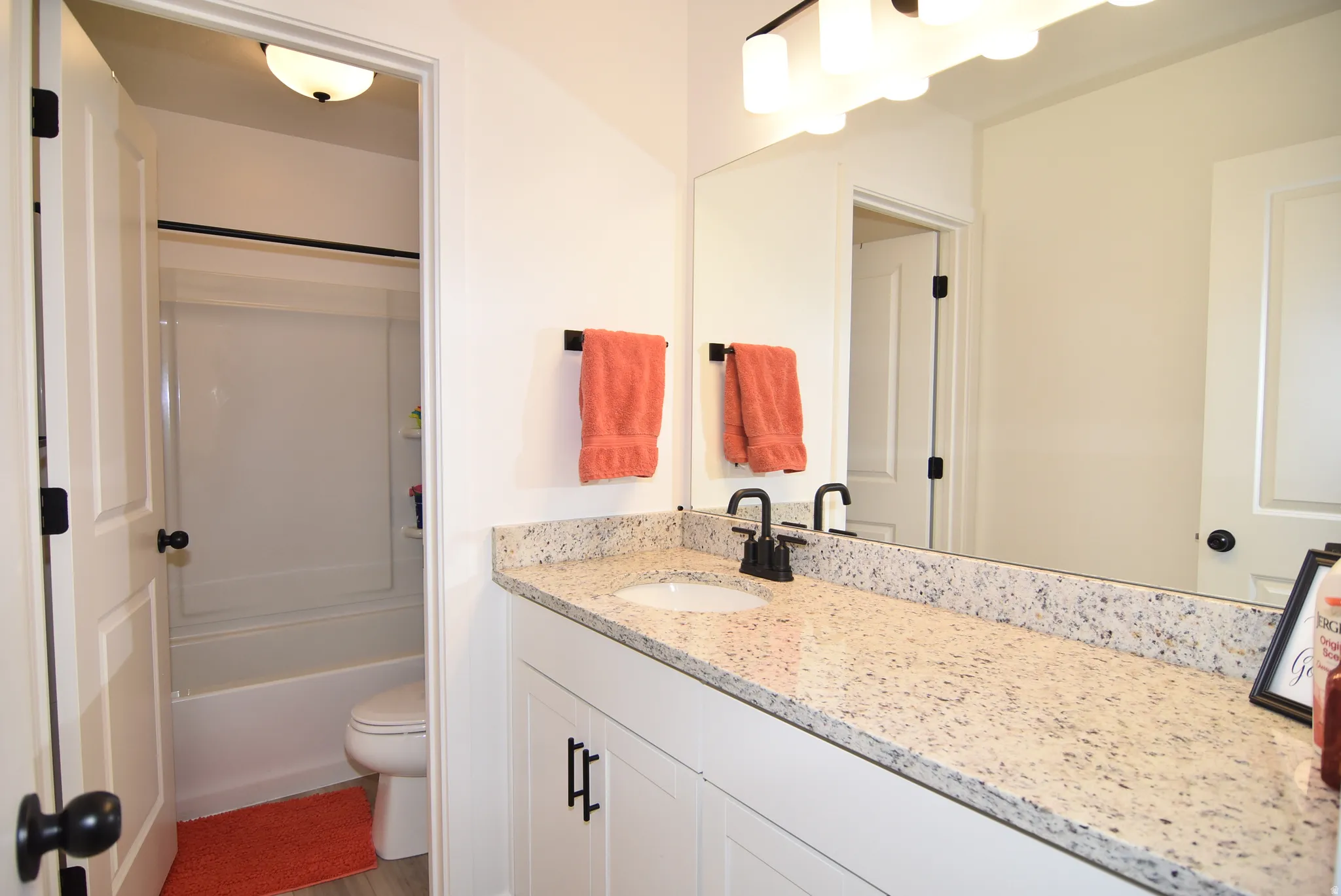 Bathroom #2 featuring a light-colored speckled countertop, white cabinetry with dark hardware, a single basin sink with a dark-finish faucet, and a large wall mirror