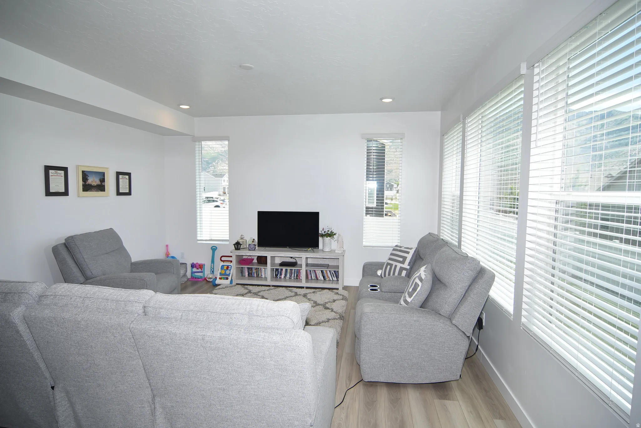 Open-concept living space featuring light wood-finish flooring, recessed lighting, and multiple windows with blinds