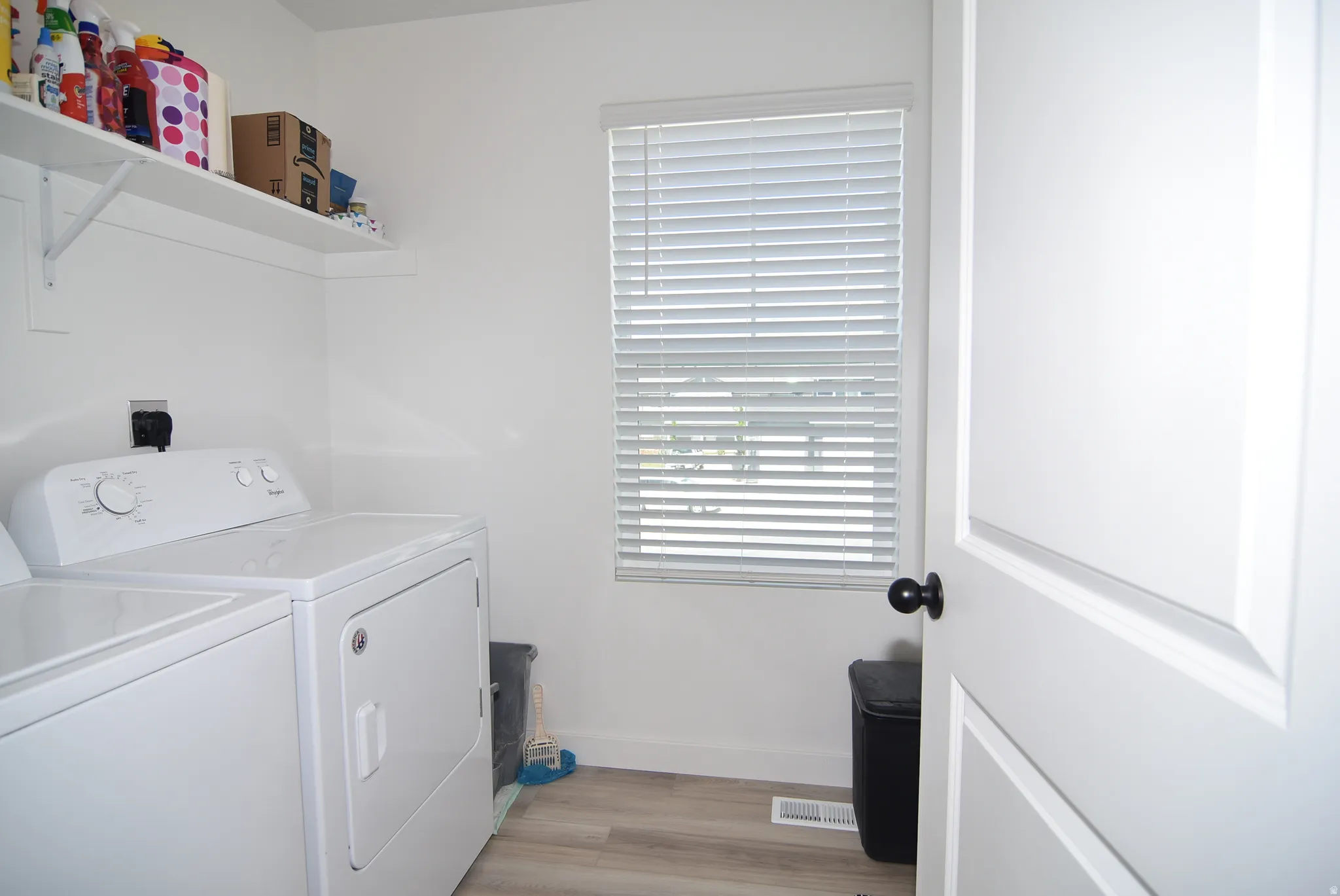 Dedicated laundry space featuring a window with horizontal blinds, wood-finish flooring, and a built-in wall shelf