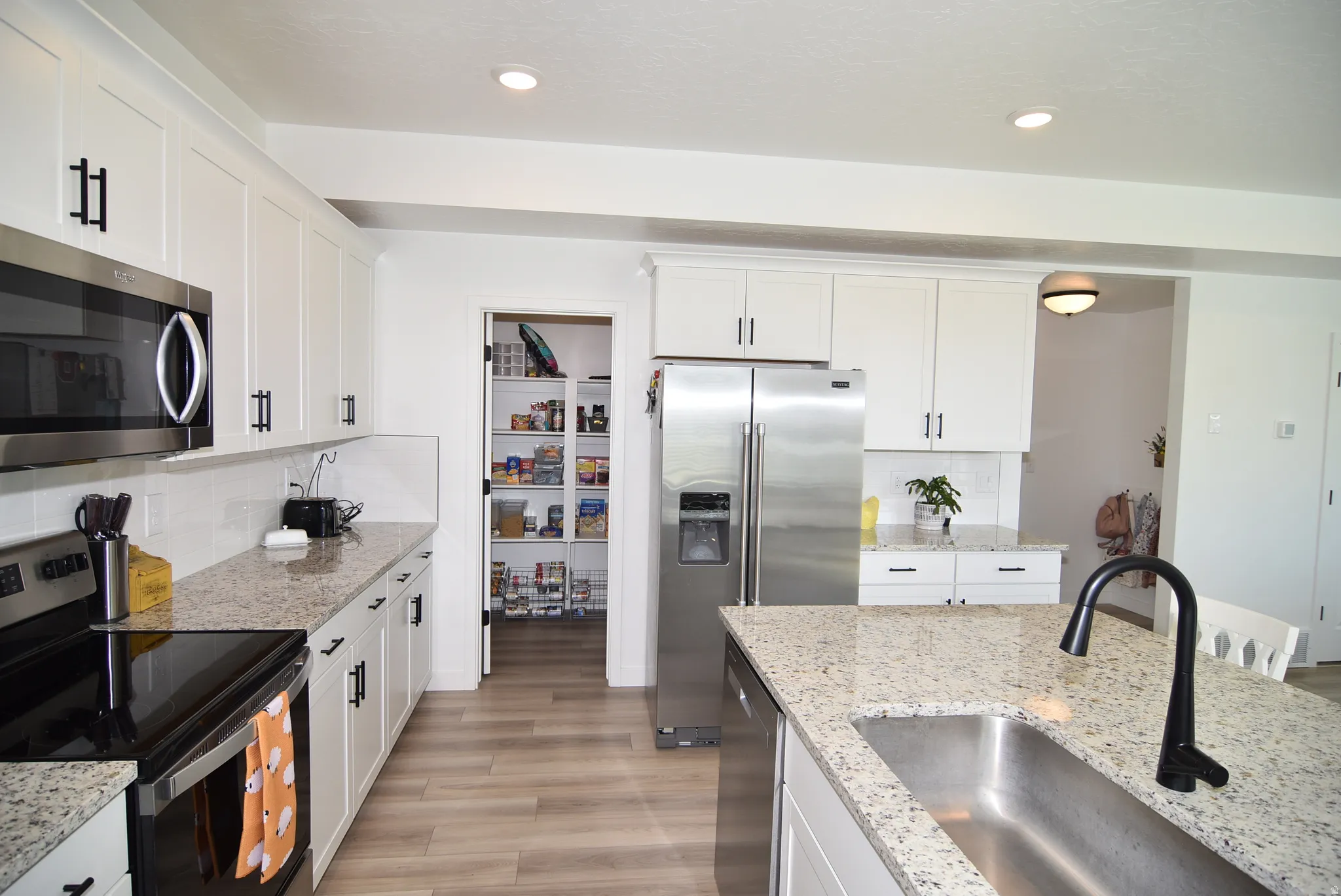 Kitchen featuring extensive white cabinetry with black hardware, wood-finish flooring, and light-toned countertops