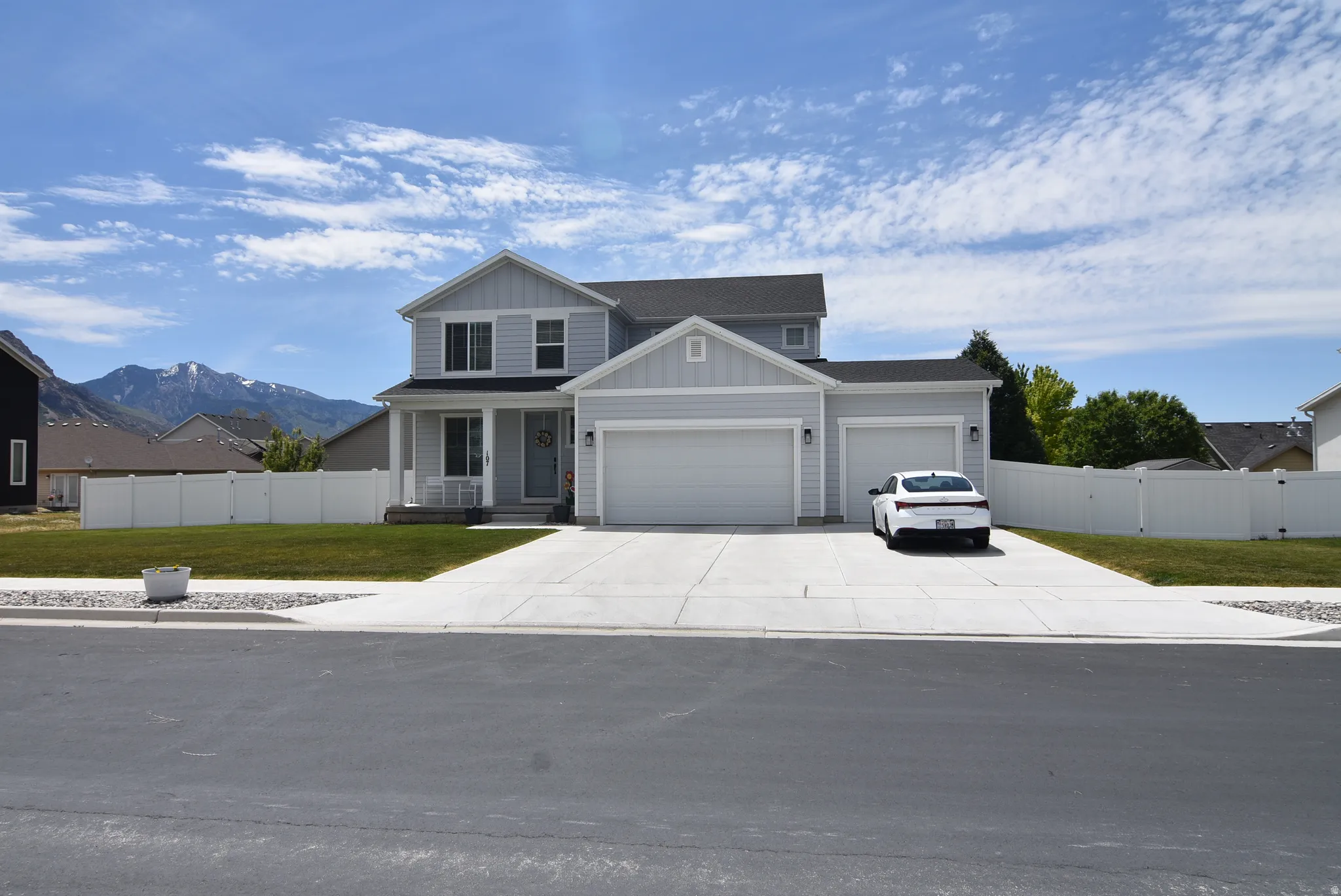 Light gray two-story residence featuring a covered front porch, a three-car garage, and a concrete driveway