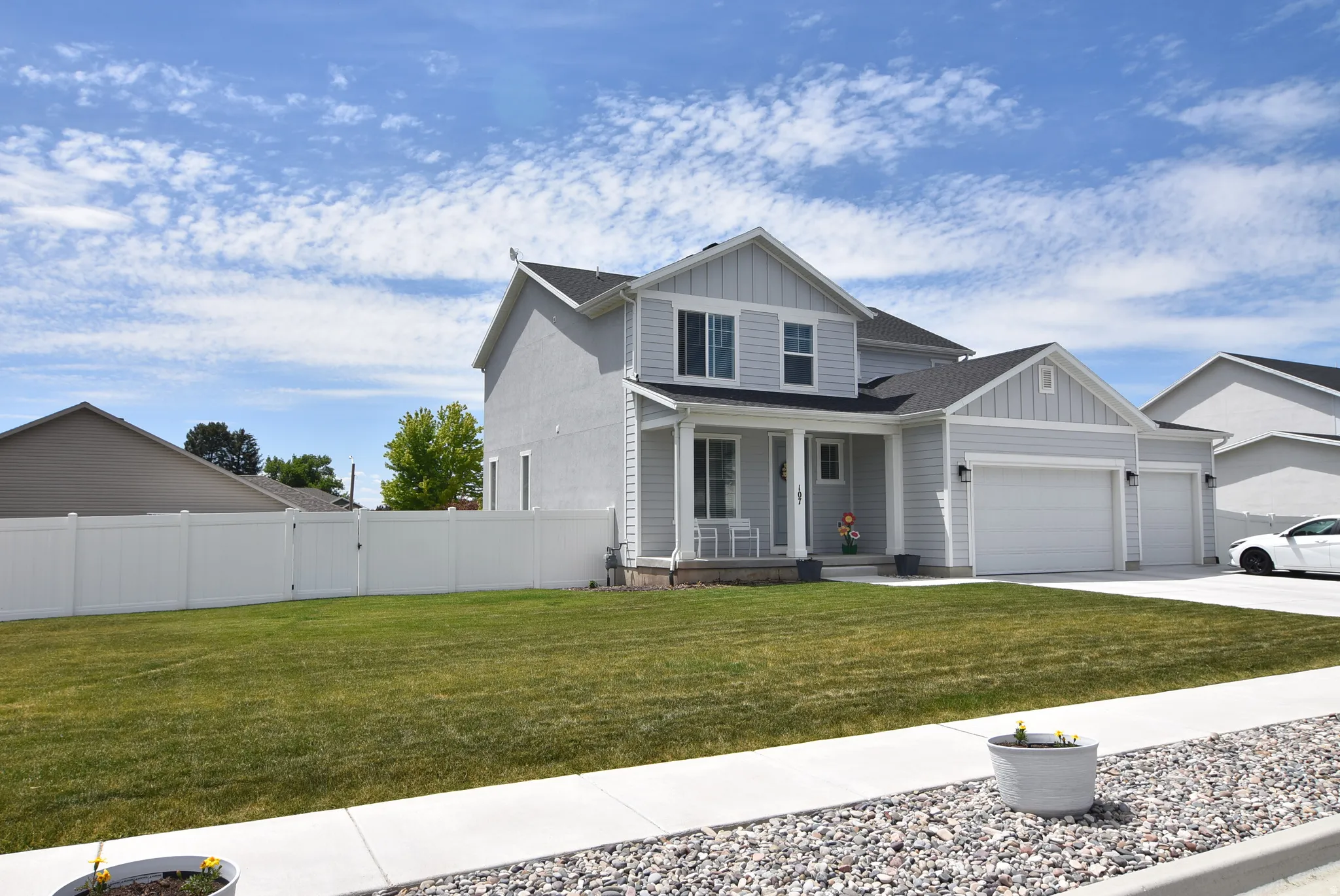 Light gray siding home featuring a covered front porch, a two-car garage, and a three-car wide driveway